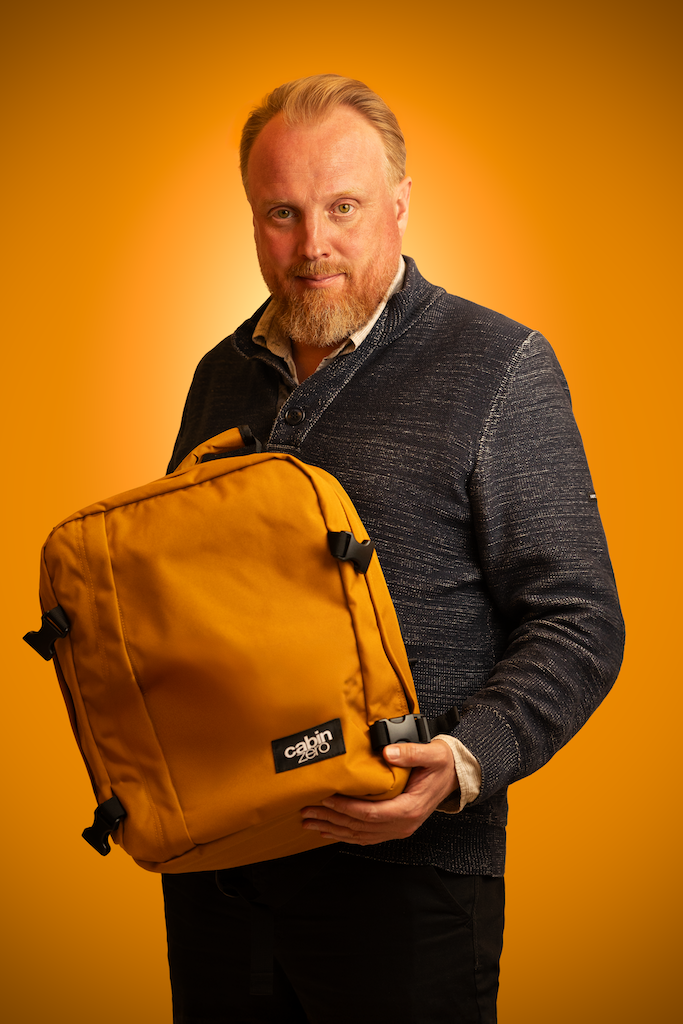 Mies esittelee okrankeltaista Cabin Zero -reppua oranssilla taustalla – Amelii Kenkä & Laukku